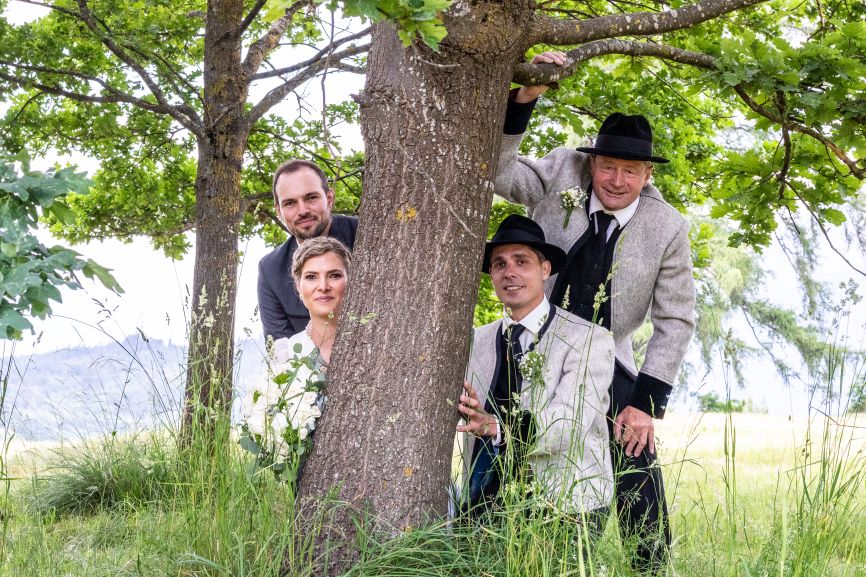 Braut und Bräutigam versteckt hinter einem Baum mit Trauzeugen